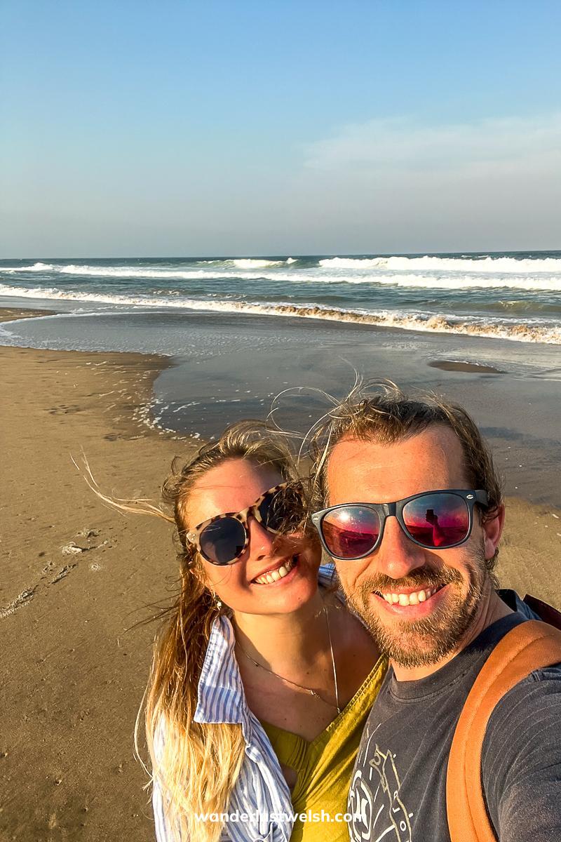A selfie of a couple on a sandy beach with choppy waves