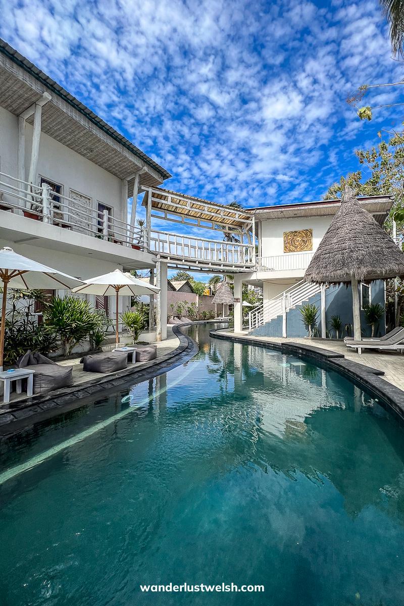 A pool running through two halves of a hotel with a small skybridge over it
