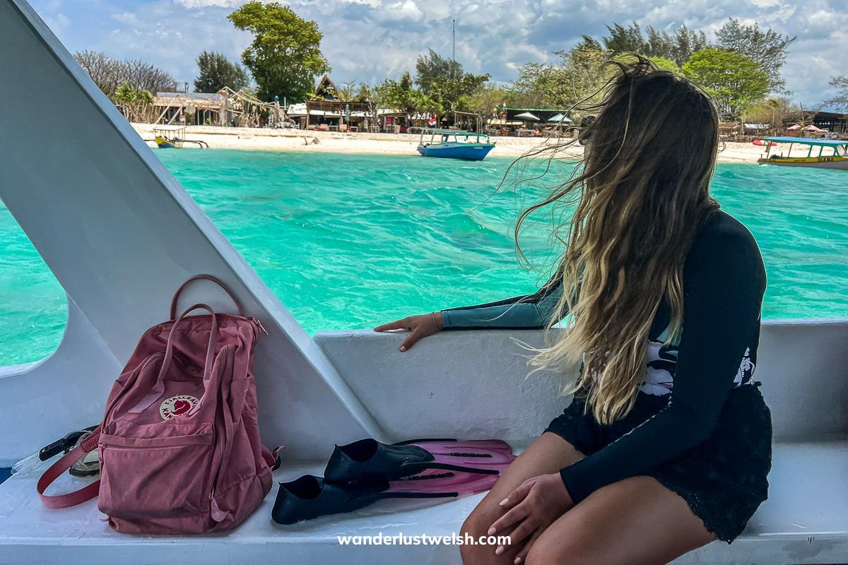 A woman in a shorty wetsuit sat on a white speedboat next to a pink backpack, looking out to the turquoise waters
