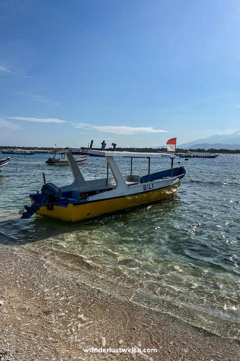 A small yellow and white wooden boat with an Indonesian flag flying