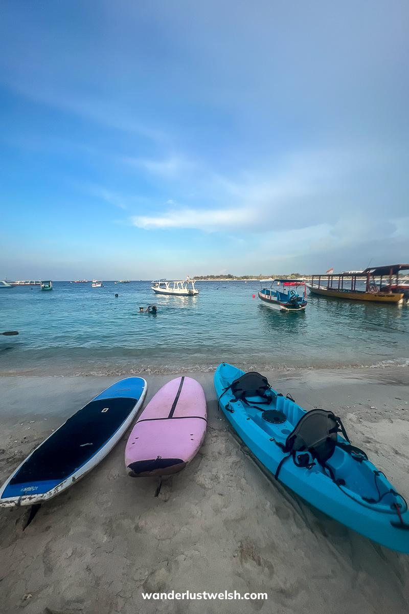 Blue and pink SUPs and sea kayaks at the water's edge on a sandy beach