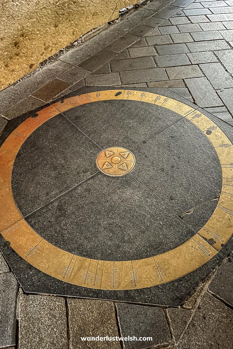 A bronze sculpture on a stone street - Circular ring with directions and distances to cities around the globe