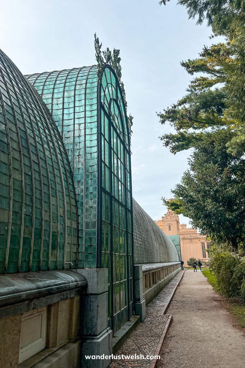 A large glass and iron framed palmhouse with a gravel path