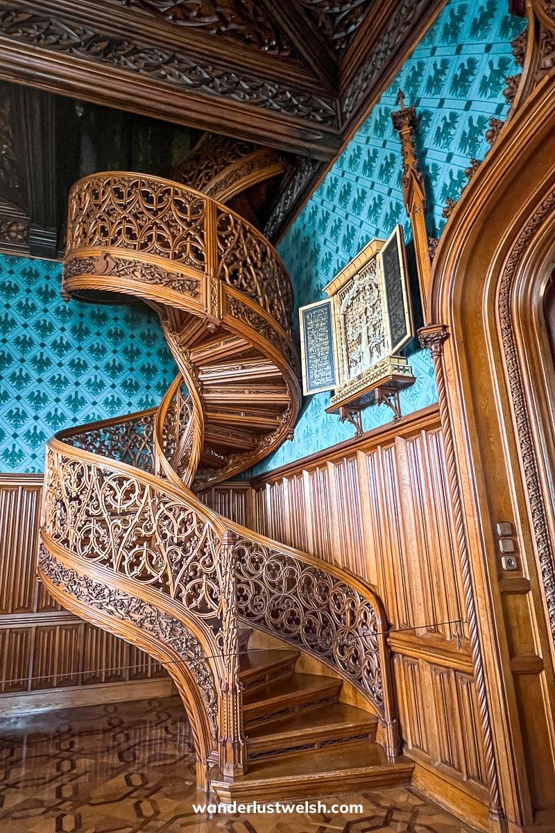 An opulent room with wooden spiral staircase and blue/teal wallpaper