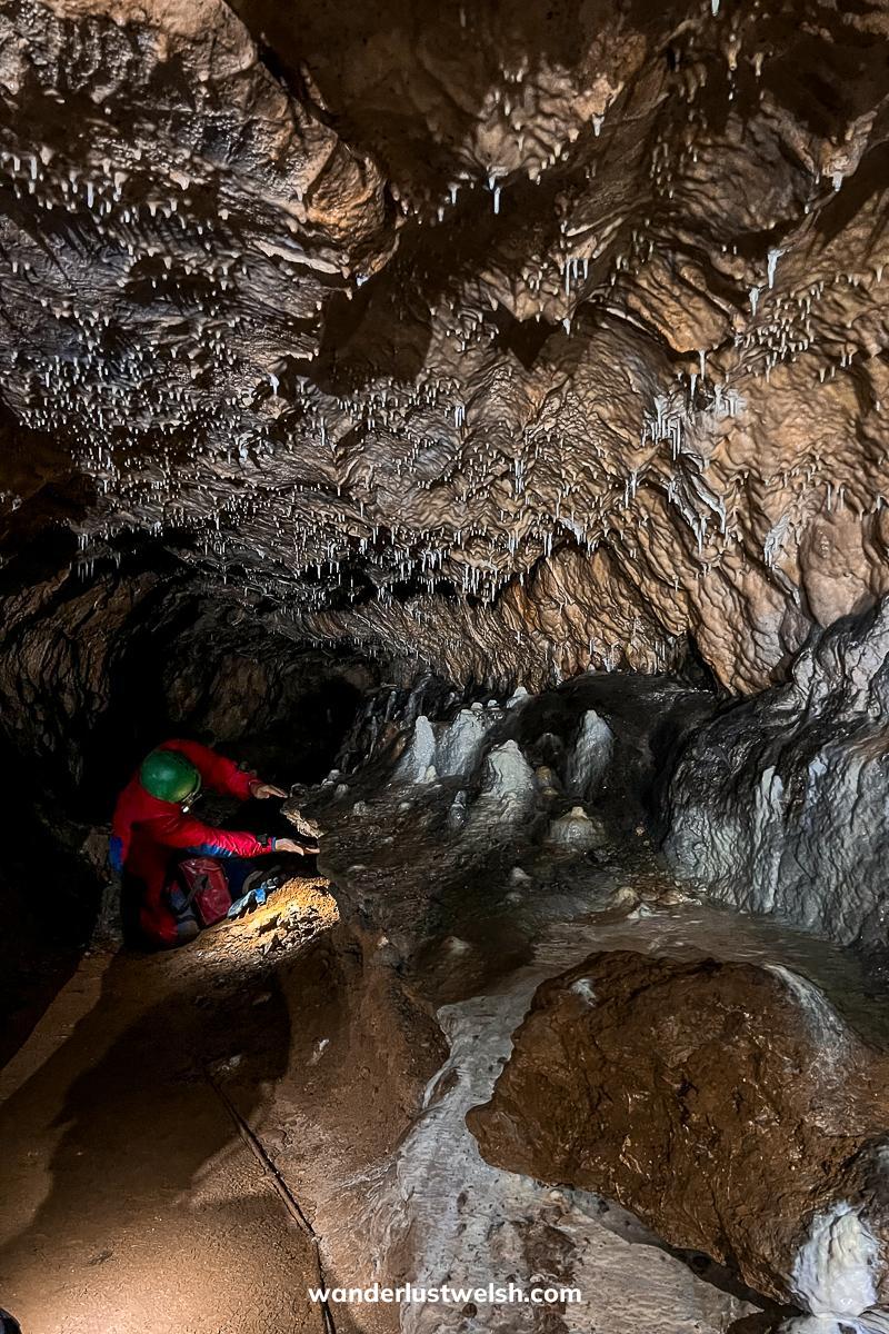 Someone in a boiler suit and hardhat crouching down in a cave