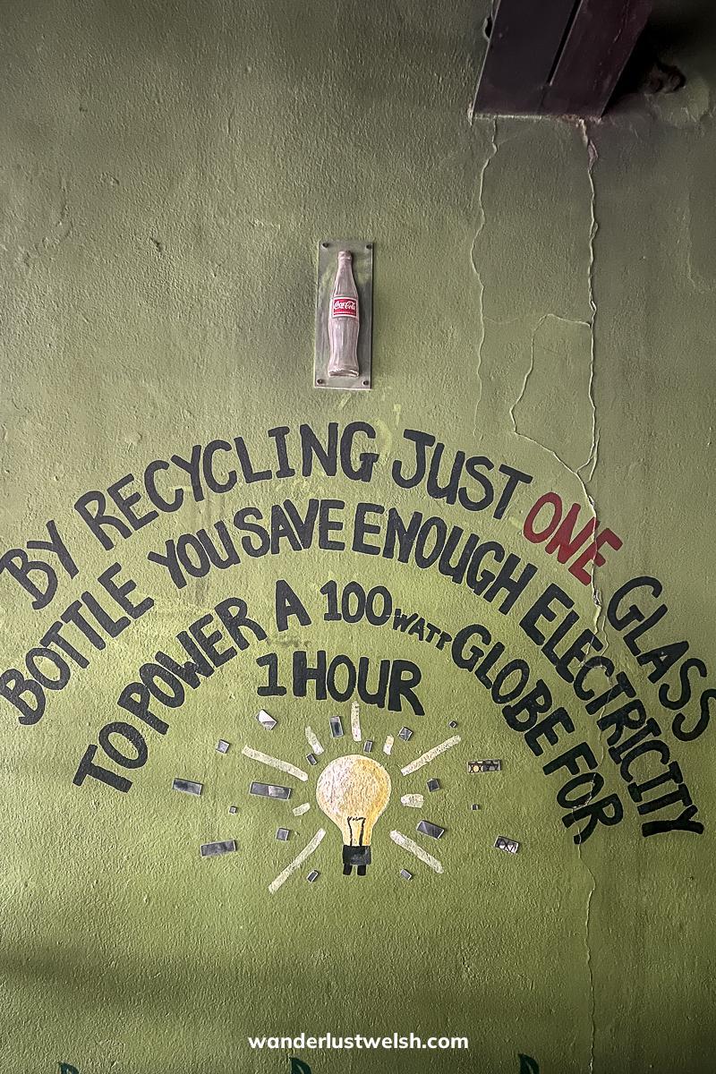 A glass bottle with the words "By recycling just one glass bottle you save enough electricity to power a 100watt globe for 1 hour" painted on the wall