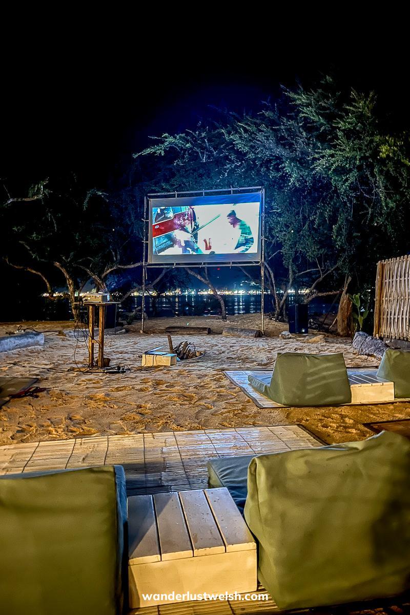 Bean bags on the beach facing a large outdoor cinema screen