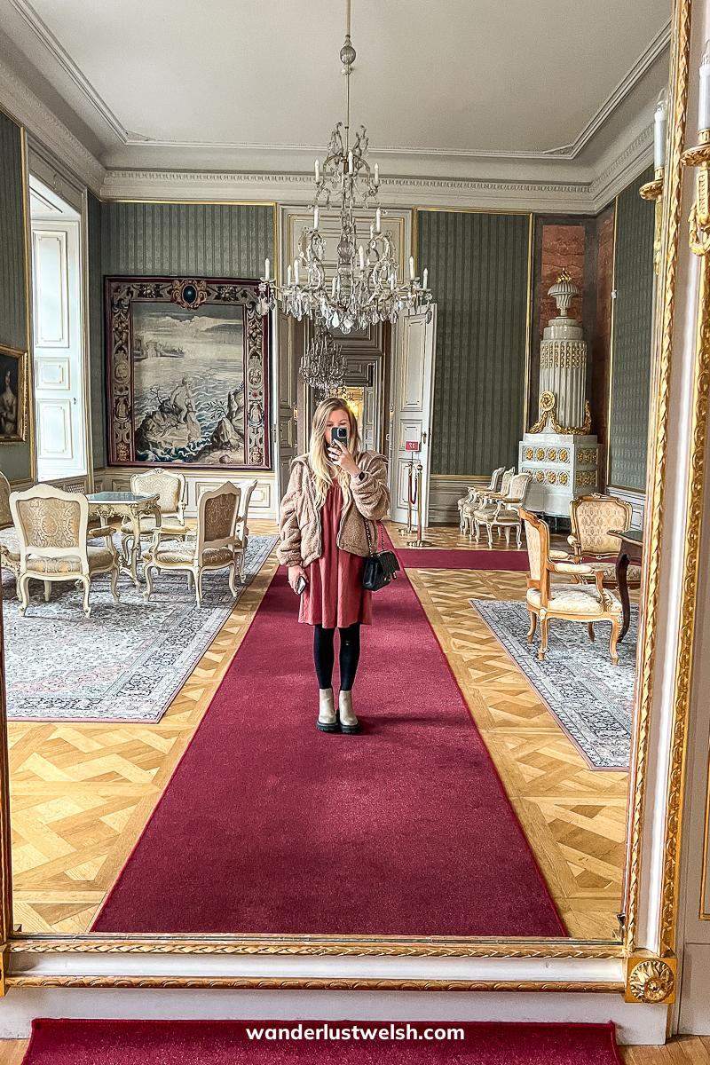 A woman taking a photo of her reflection in a palace room on a red carpet