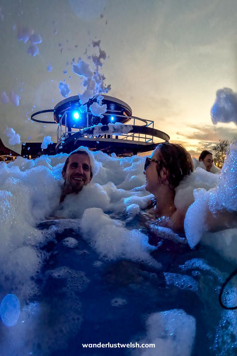 A couple in a pool surrounded by foam and more foam being blasted out from above