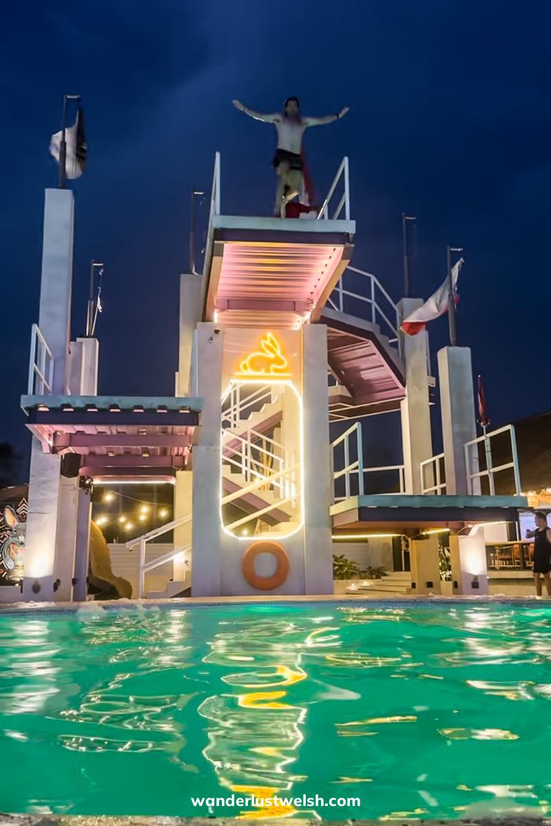 A man jumping from a 10m high dive board lit up in yellow and pink