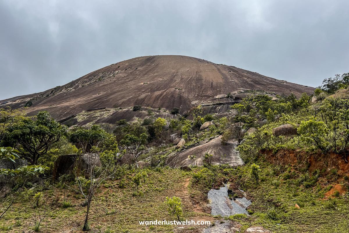 Sibebe Rock - A large single rock mountain surrounded by grass, shrubs, and trees