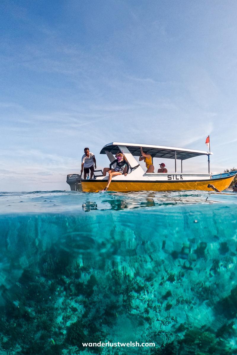 A water level photo showing a woman about to jump from a boat above and the coral reef below