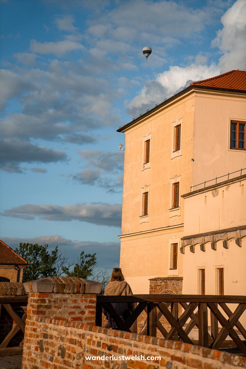 A woman watching a hot air balloon flying above Spilberk Castle
