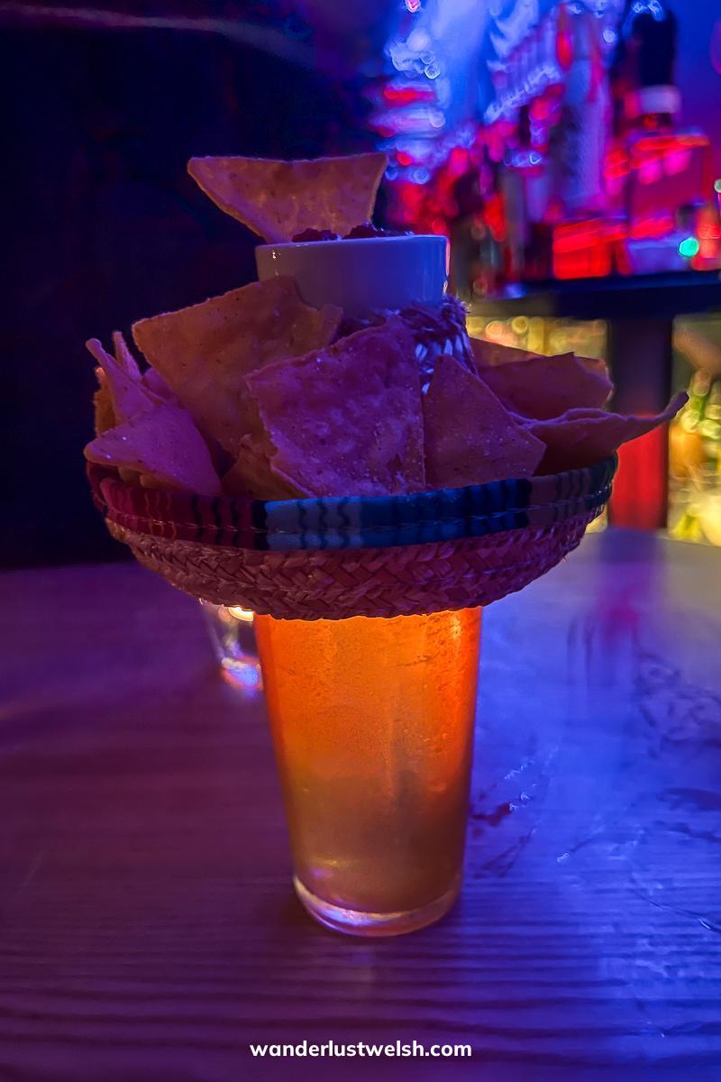 A cocktail with a ceramic sombrero on top holding nachos