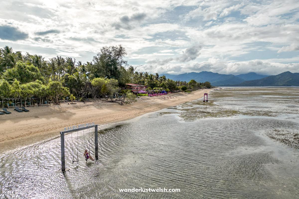 A drone shot of a woman on a swing in the shallow sea