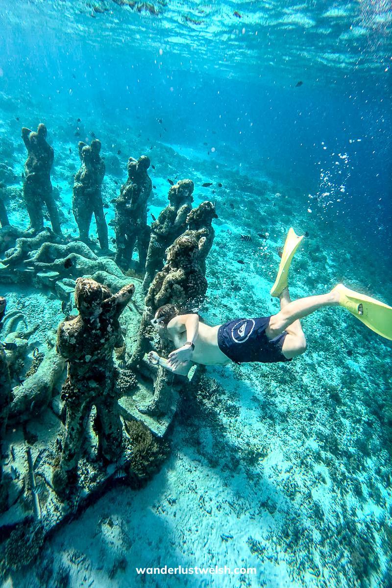 A man in yellow fins diving down to underwater statues in the Gili Islands