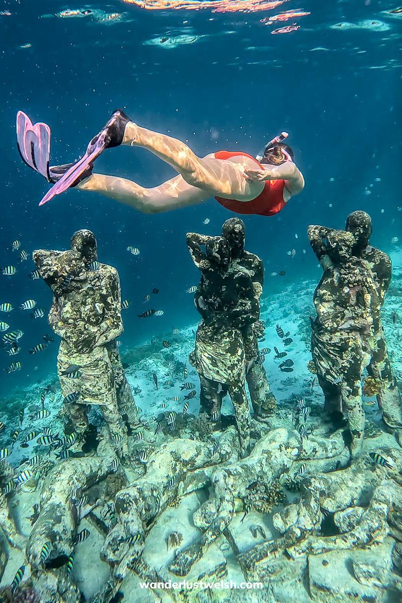 A woman with pink fins diving down to underwater statues in the Gili Islands
