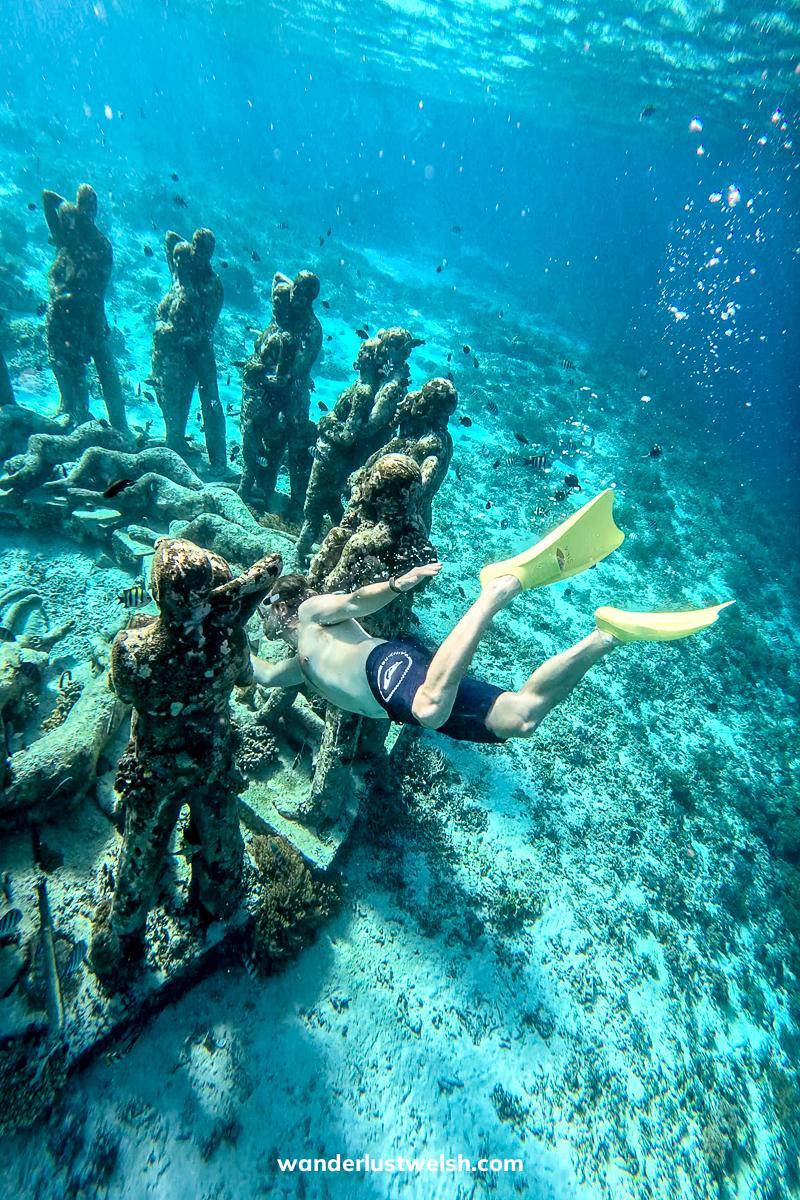 A man in yellow fins diving between underwater statues
