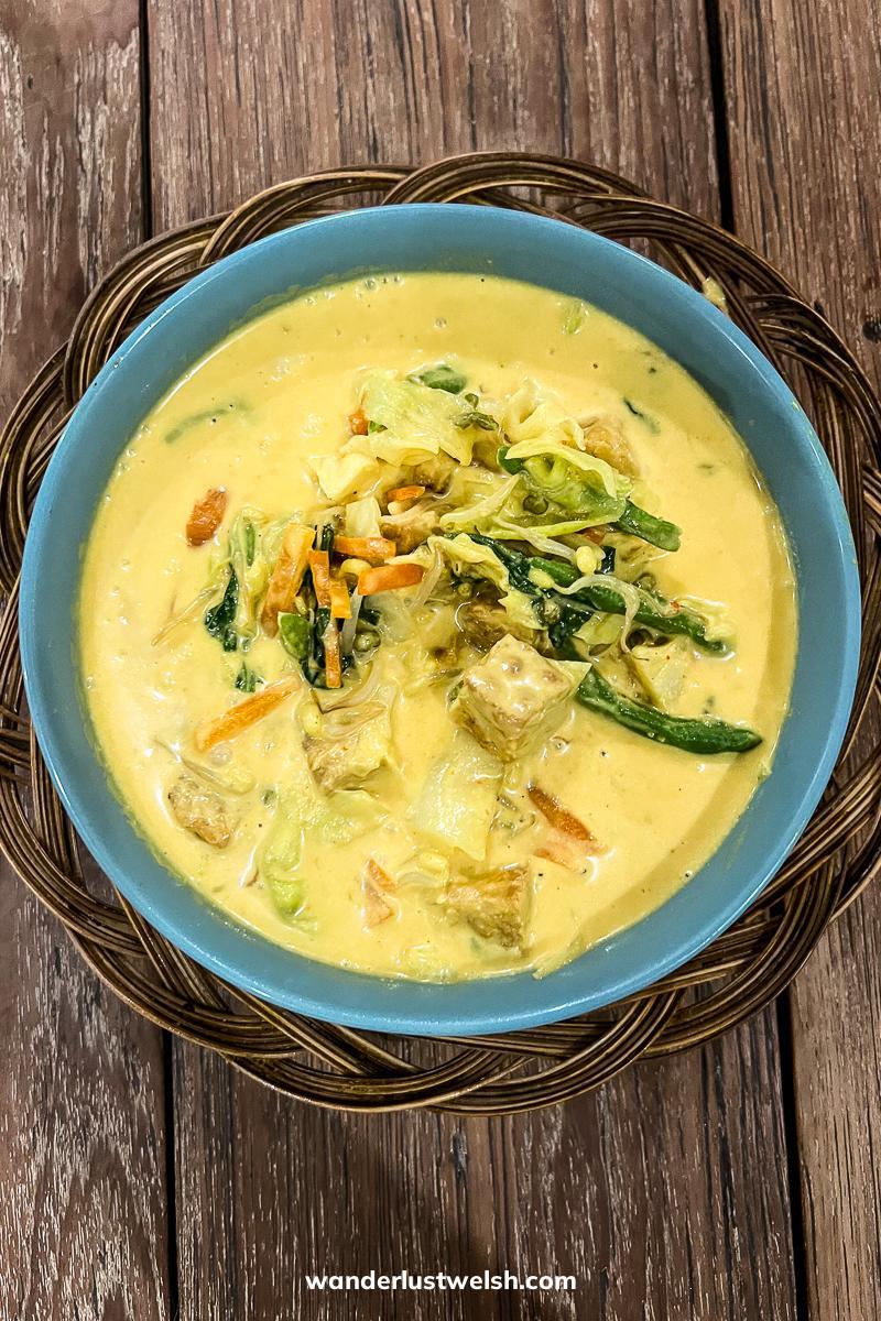 A yellow tofu curry in a blue bowl on wooden table