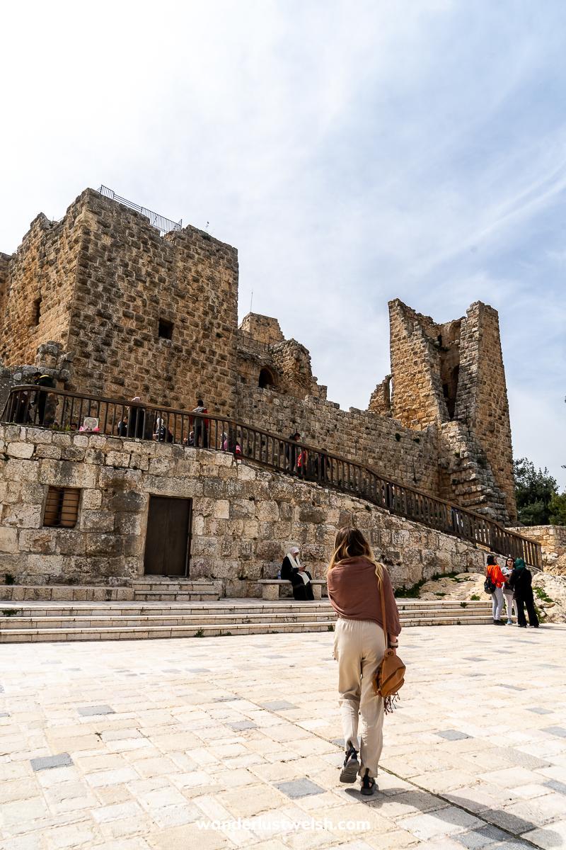 A woman walking through a white stone courtyard with a large castle in the background