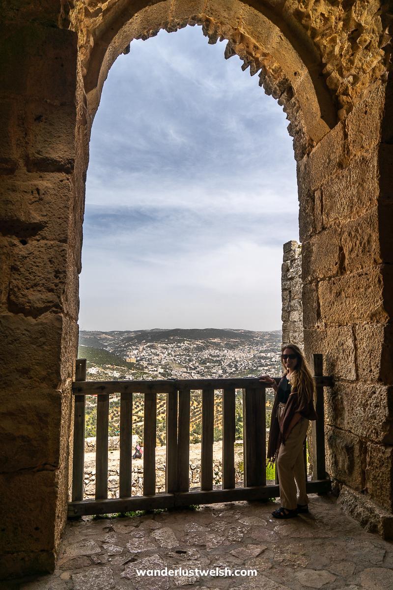 A woman in a large stone arch balcony looking out over the northern Jordan landscape