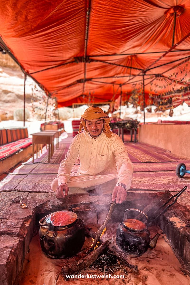 A Bedouin man making tea using traditional wood fire in a large tent in the desert