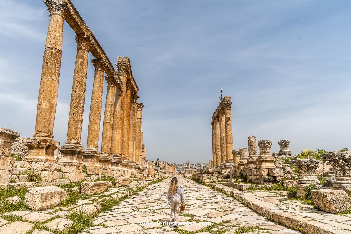 A woman walking down a Roman Road in Jerash flanked by large Roman columns