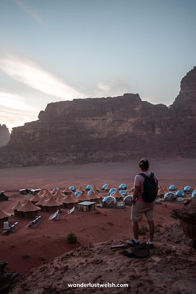 A man standing looking at a resort in the desert resembling a Martian colony with glass domes
