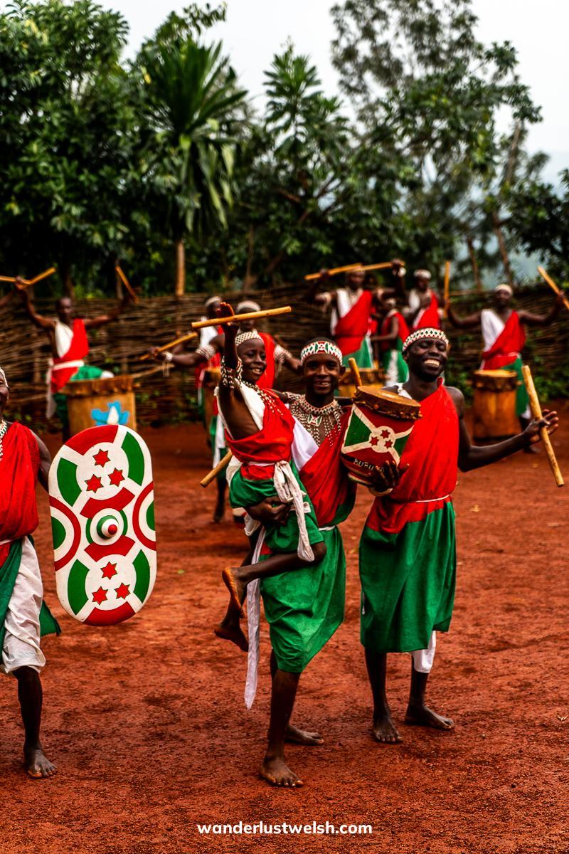 A boy being held up at the Gitega Drum Sanctuary surrounded by drummers in colorful outfits