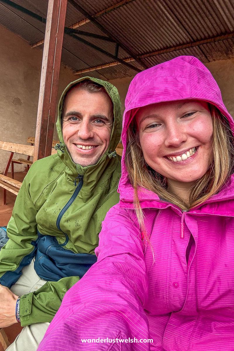 A couple in rain jackets and hoods under cover in the Gitega Drum Sanctuary
