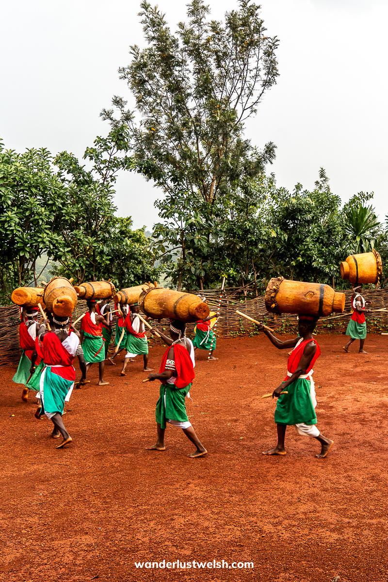 A group of men in red, green, and white outfits carrying large drums on their heads