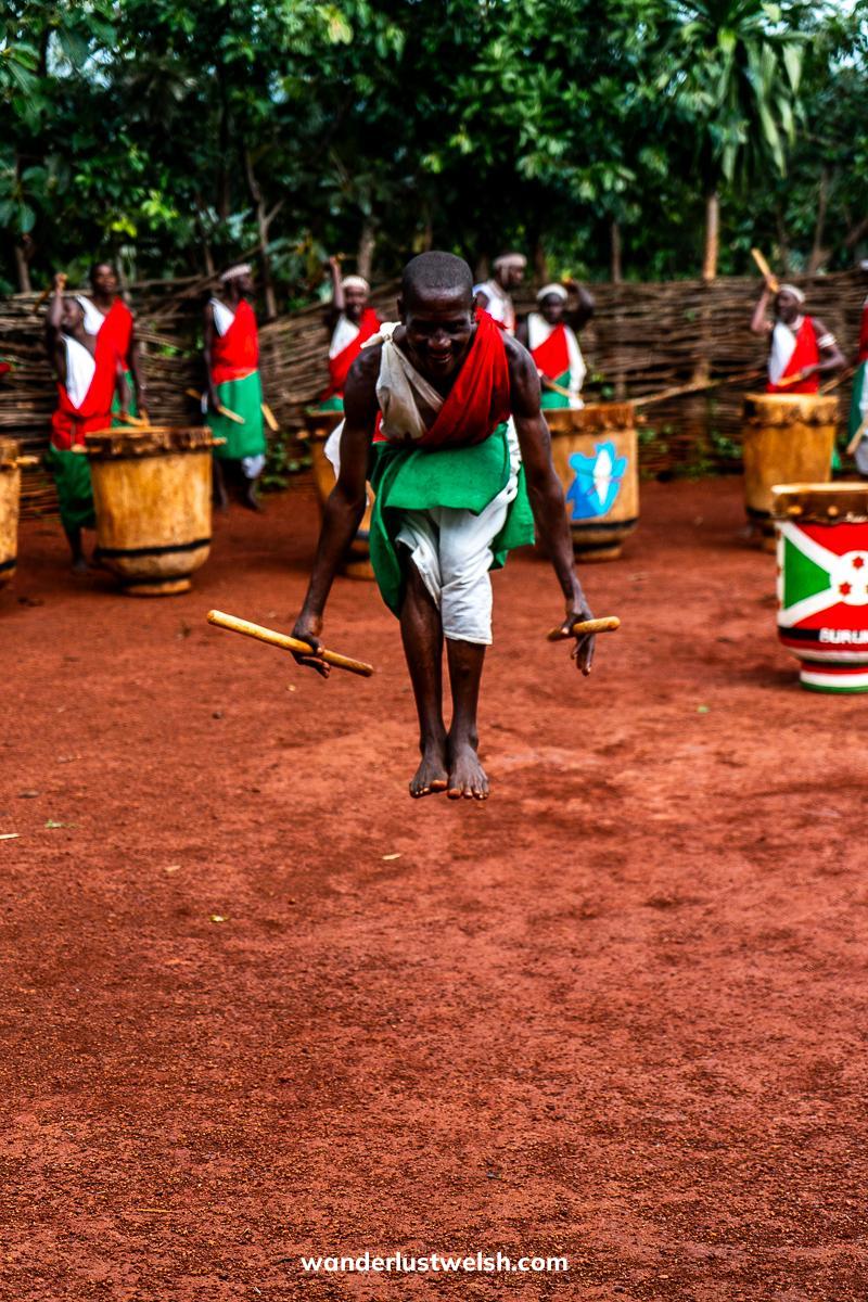 A man surrounded by drummers in Burundi outfits jumping high at the Gitega Drum Sanctuary