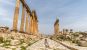 A woman walking along a wide Roman road with large columns on either side