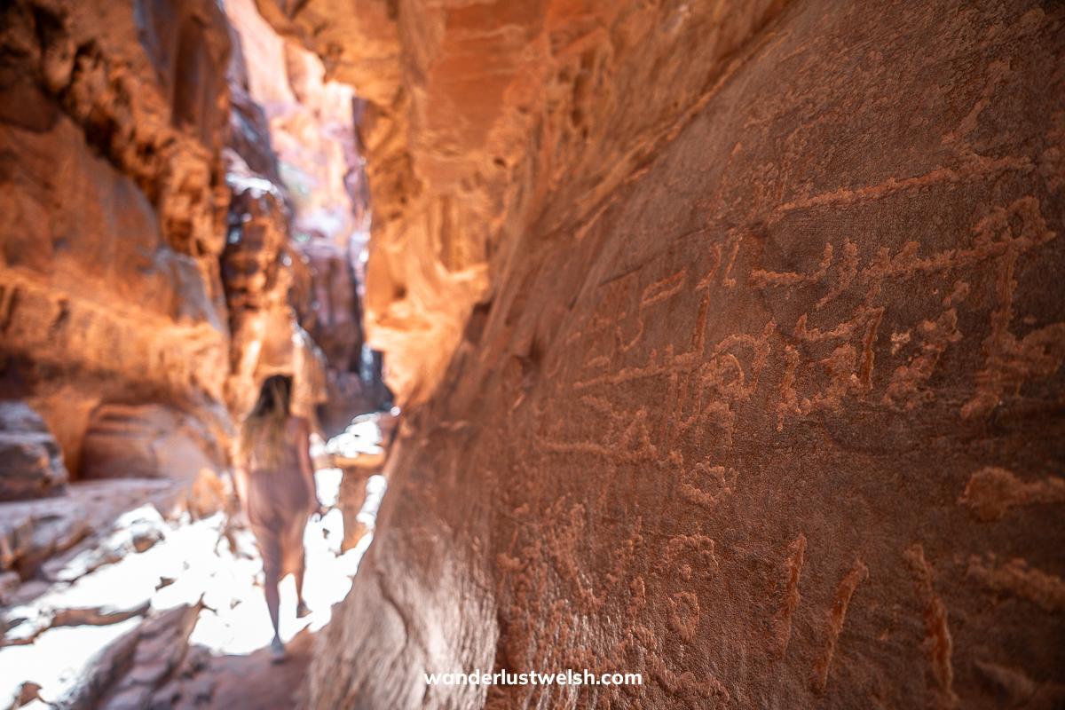 Rock carved inscriptions in Wadi Rum with a woman walking in the background