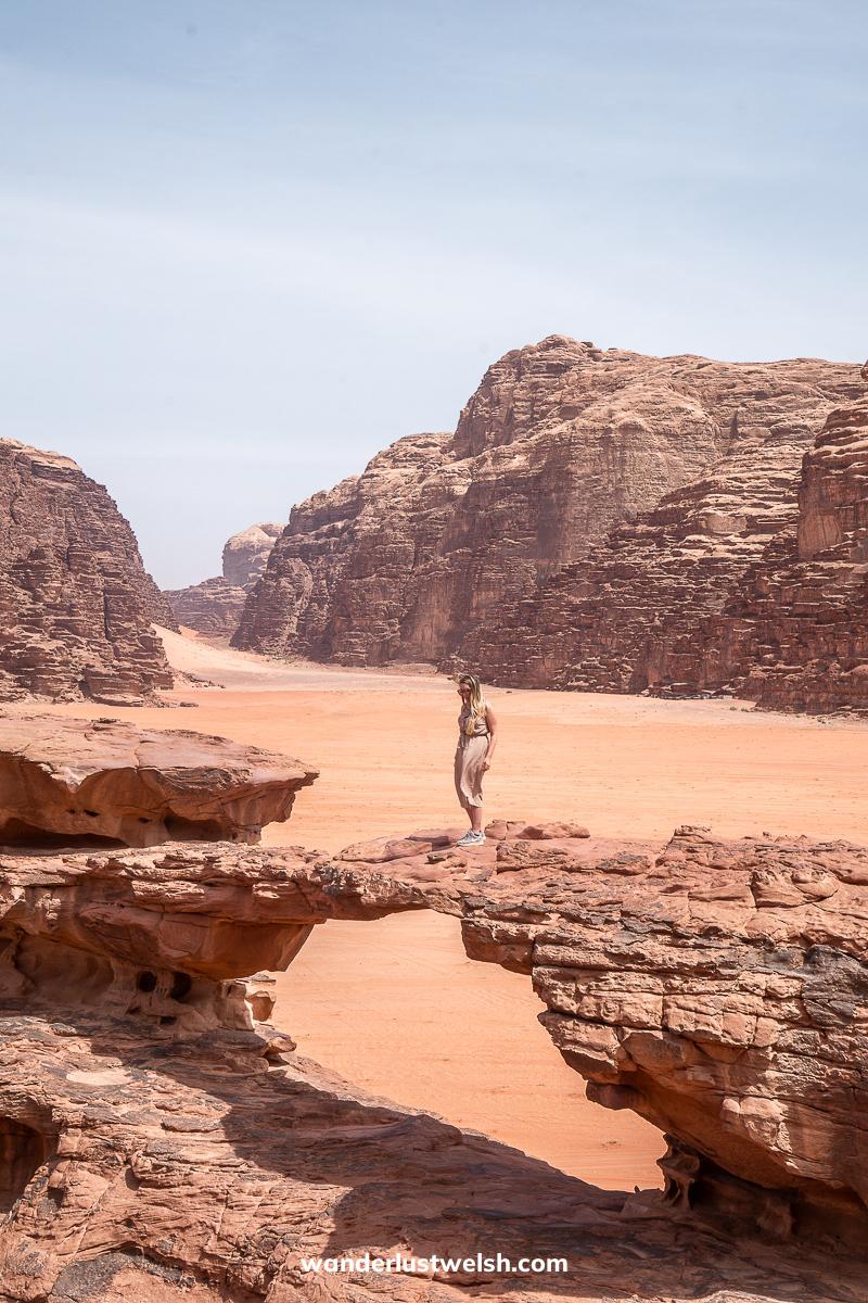 A woman standing on a small rock arch in Wadi Rum