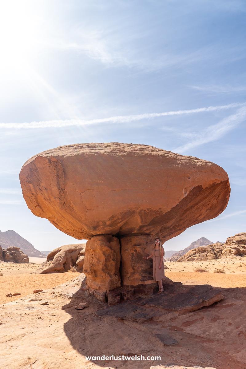 A woman standing in the shade of a large mushroom shaped rock in the desert