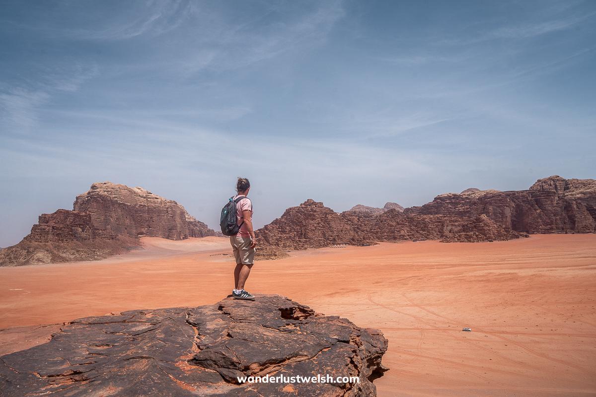 A man standing on a rocky viewpoint overlooking the red sands of Wadi Rum
