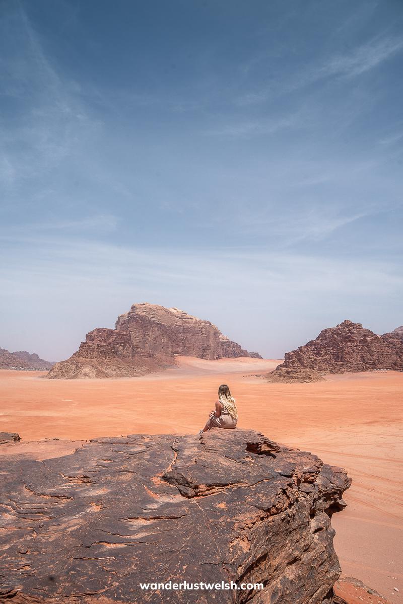 A woman sitting on a rocky viewpoint overlooking the red sands of Wadi Rum