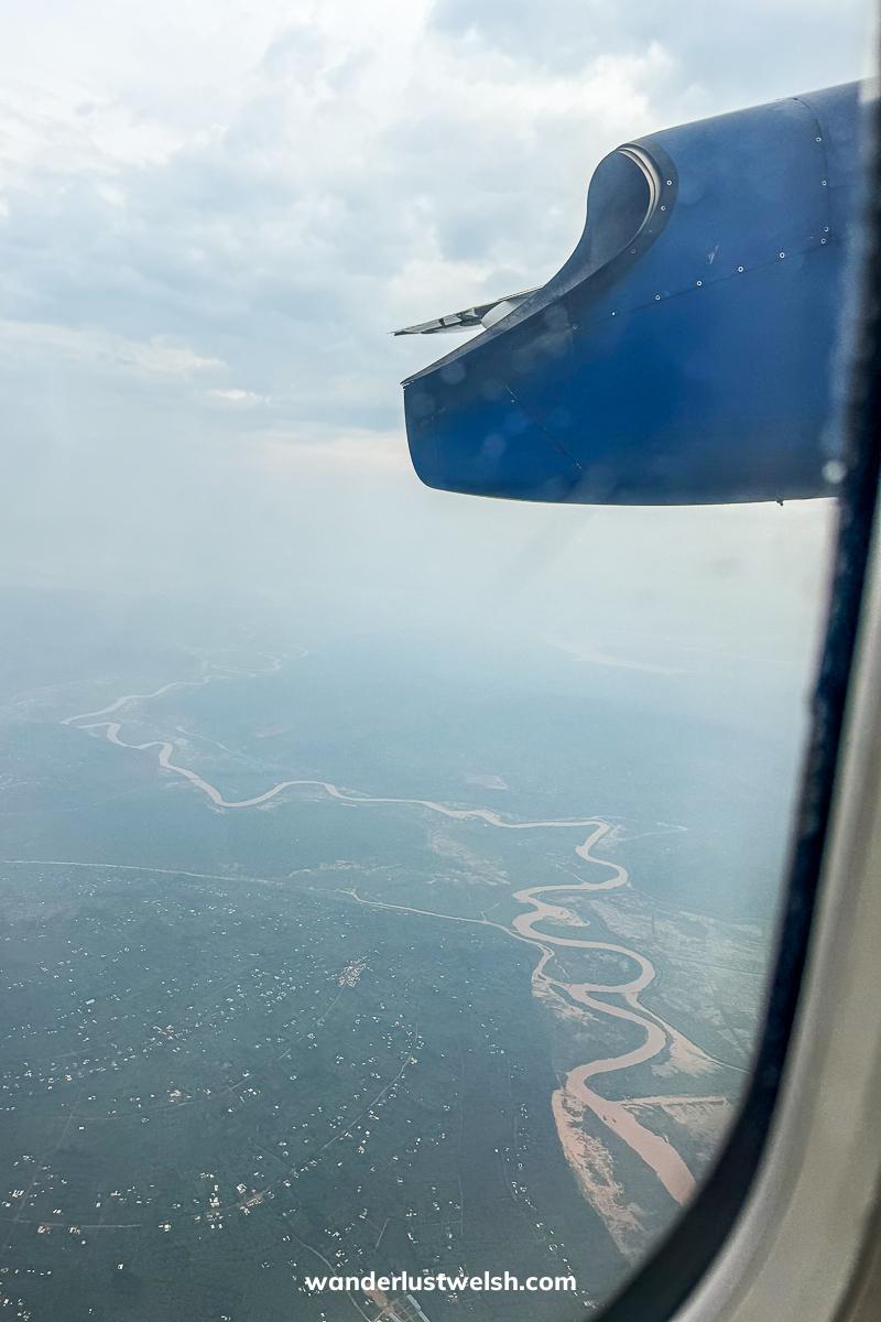 A large, muddy river winding through a thick rainforest from a plane window