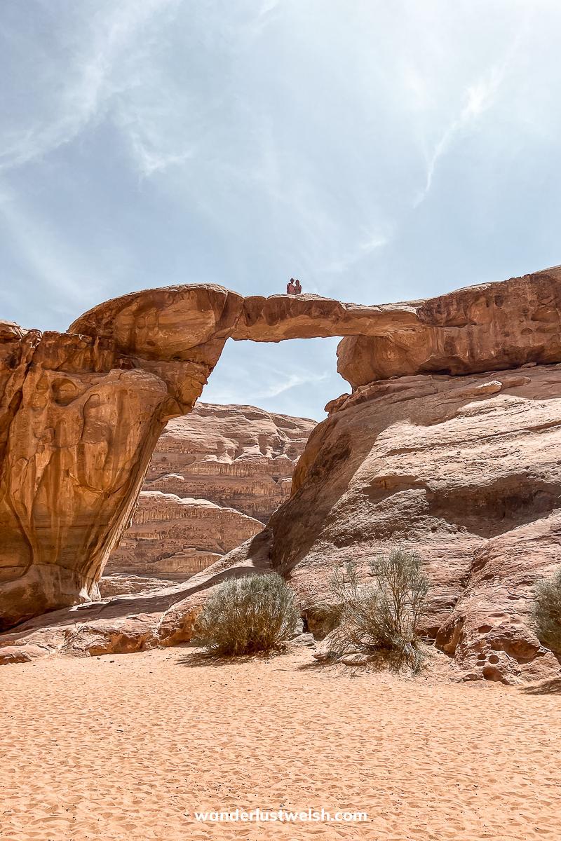 A couple standing on top of a huge natural rock arch in a desert