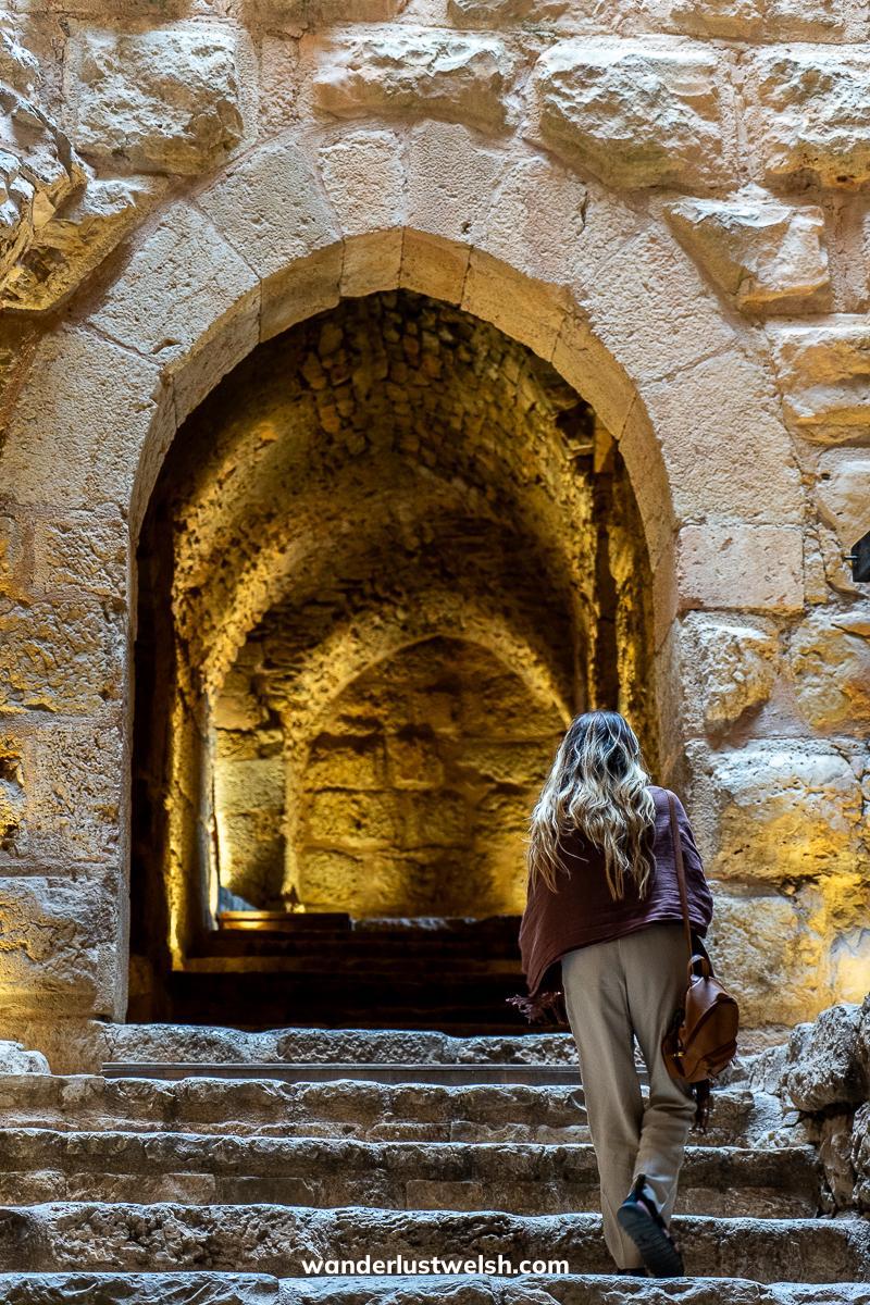 A woman walking through an arched entranceway to Ajloun Castle