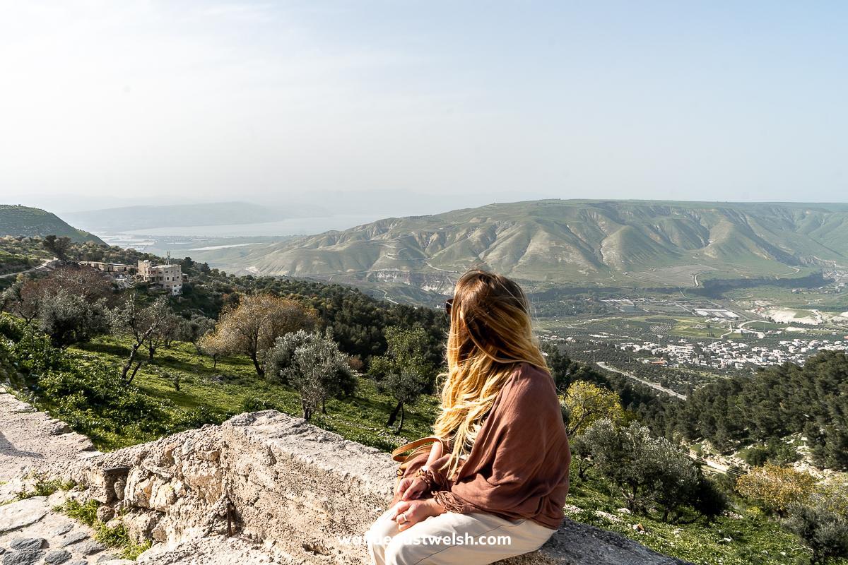 A woman sitting on a stone wall looking out over the northern Jordan landscape and the Sea of Galilee